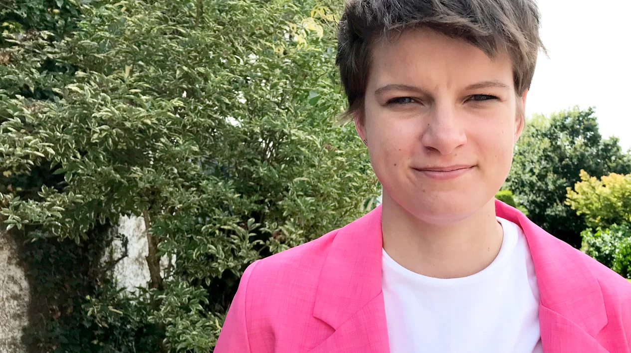 Head and shoulder portrait of a young woman with short hair and a bright pink jacket in a park