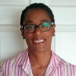 Smiling black woman with short hair and black glasses wearing a stripey pinks and white shirt.