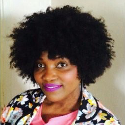 Head and shoulder portrait of a smiling African woman with a big afro, wearing a colourful bright patterned top.