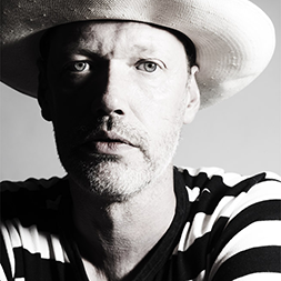 Monochrome head and  shoulder portrait of a white male wearing a hat and black and white striped jumper