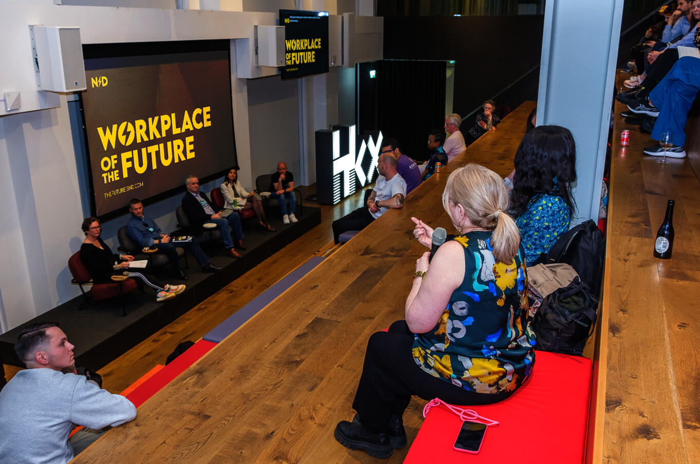 Event space with a panel discussion for 'Workplace of the Future.' Speakers are seated on stage with the 'Workplace of the Future' logo on a screen behind them. Audience members are engaged, listening to the conversation on neurodiversity in the workplace.