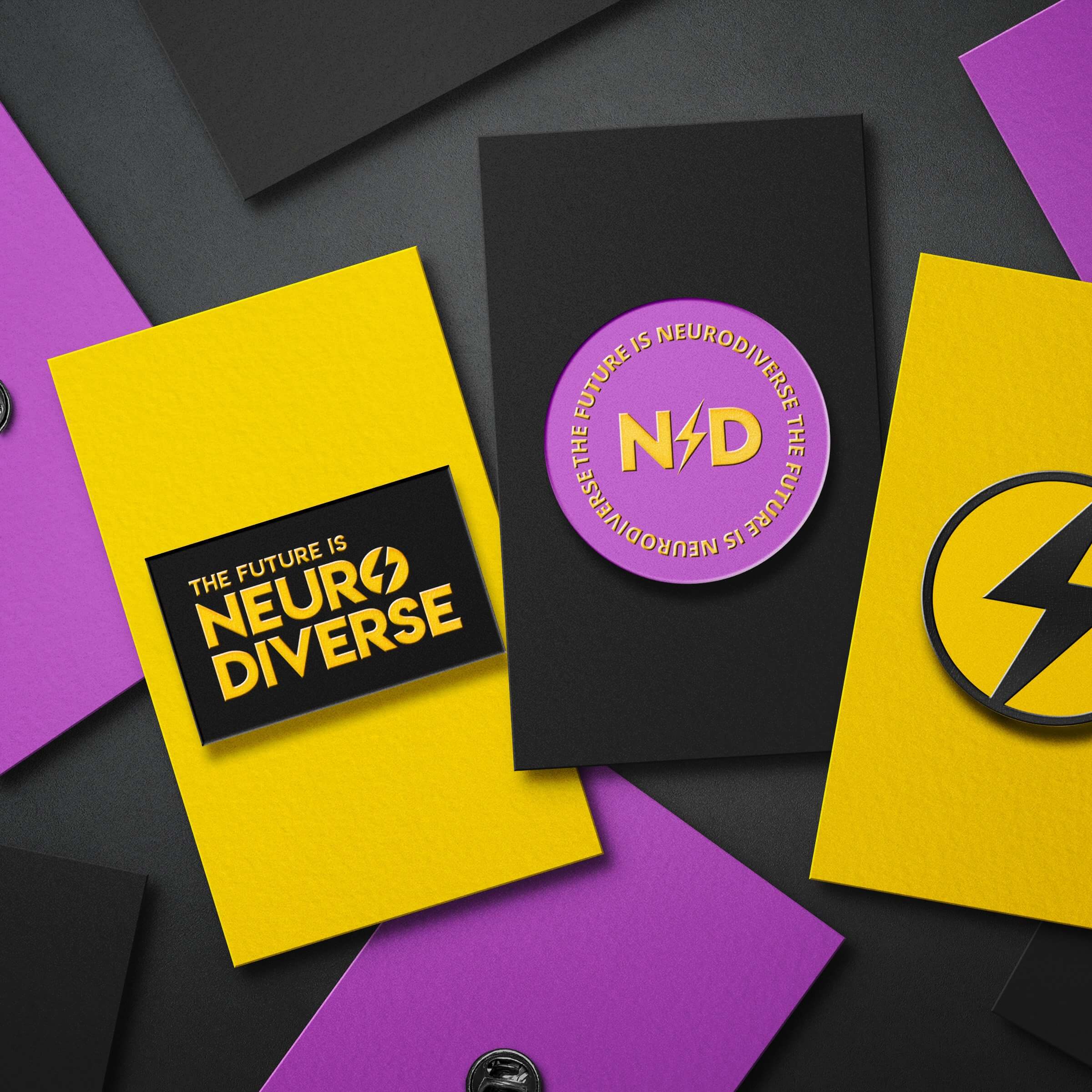 Close-up of ND-branded badges and cards featuring 'The Future is Neurodiverse' logo with lightning bolt and vibrant colours in yellow, black, and purple. Designs reflect a bold and inclusive brand identity.